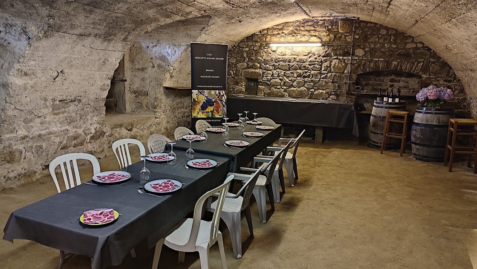 Cave voûtée en pierre préparée pour une dégustation, tables dressées et tonneaux